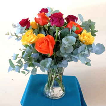 Vibrant bouquet of orange, yellow and magenta roses with eucalyptus in a clear glass vase