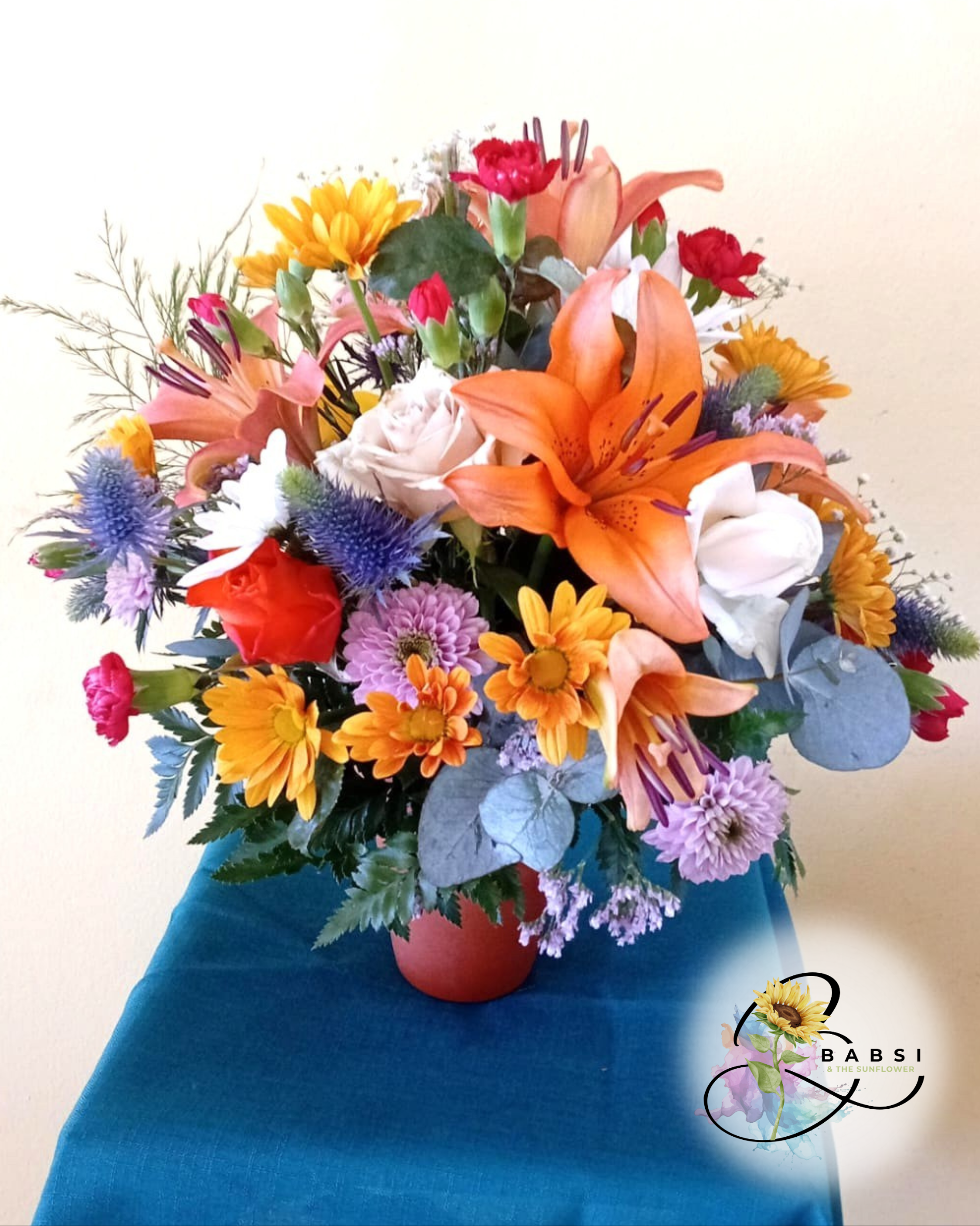Vibrant Autumn arrangement in a terracotta pot, with orange lilies, roses, gerberas & purple flowers