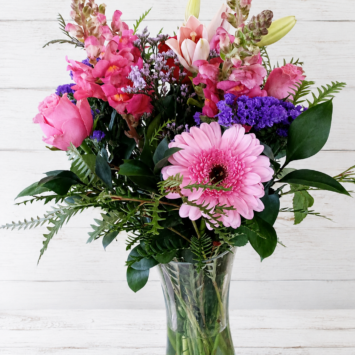 light pink and cerise roses, single lily, gerbera, snapdragons with purple statice and limonium with greenery